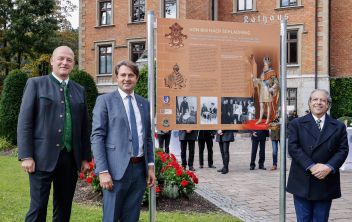 Bürgermeister DI Hermann Trinker, Landtagsabgeordneter Ing. Gerald Holler, BA und S.E. Nelson Antonio Tabajara de Oliveira, Botschafter von Brasilien in Österreich beim Enthüllen der Coburg-Tafel im Rathauspark zu sehen.
