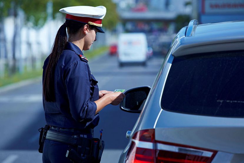 Eine Polizistin kontrolliert während einer Anhaltung die Fahrzeugpapiere eines Lenkers.